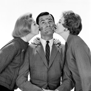 1950s TWO WOMEN KISSING SINGLE MAN ON OPPOSITE CHEEKS HIS FACE COVERED WITH LIPSTICK MARKS